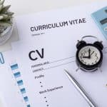 Documents CV et Curriculum Vitae posés sur un bureau avec un réveil, une calculatrice et un stylo