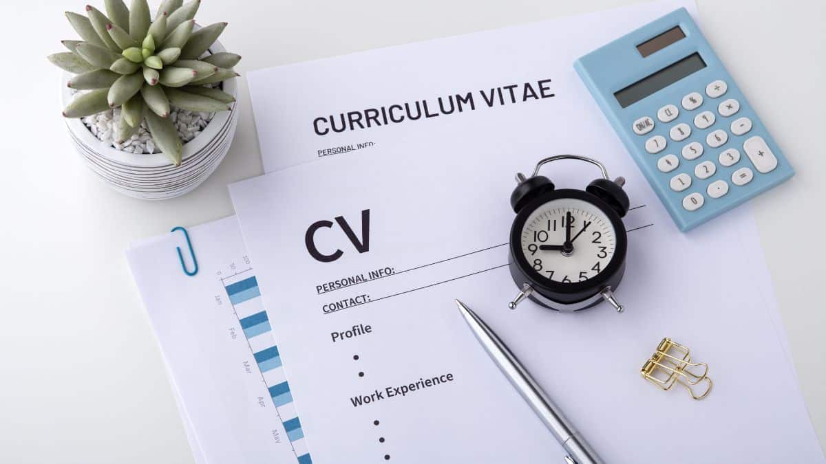 Documents CV et Curriculum Vitae posés sur un bureau avec un réveil, une calculatrice et un stylo